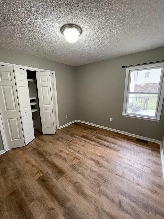 unfurnished bedroom with a textured ceiling, wood finished floors, visible vents, baseboards, and a closet