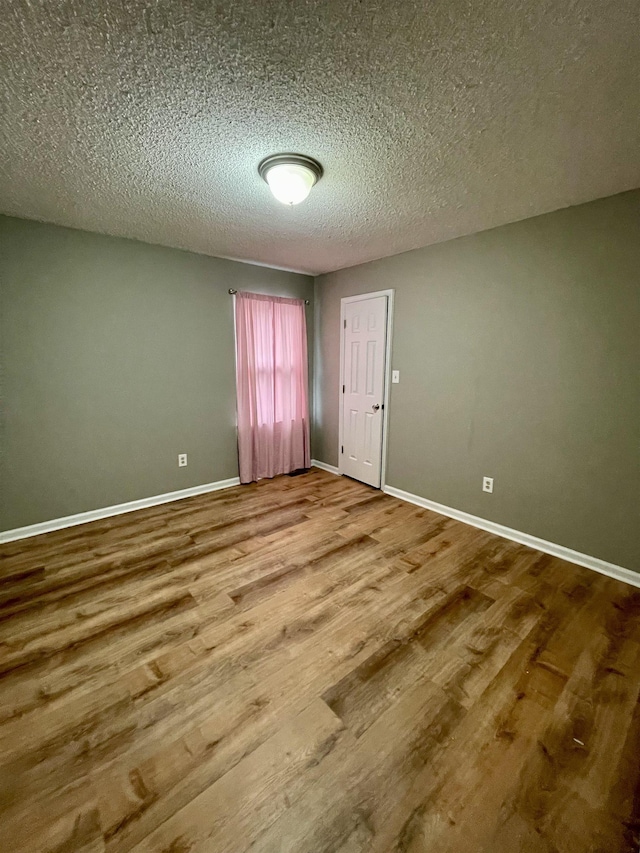 unfurnished room featuring a textured ceiling, wood finished floors, and baseboards