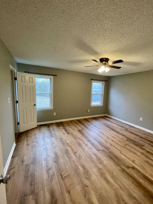 empty room with ceiling fan, a textured ceiling, baseboards, and wood finished floors