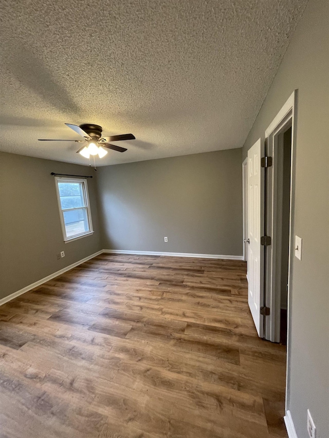 unfurnished room with a textured ceiling, dark wood-style flooring, a ceiling fan, and baseboards