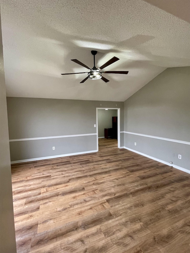 empty room featuring a ceiling fan, vaulted ceiling, a textured ceiling, wood finished floors, and baseboards