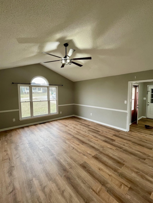 empty room featuring baseboards, lofted ceiling, ceiling fan, wood finished floors, and a textured ceiling