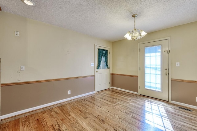 interior space featuring a textured ceiling, a notable chandelier, wood finished floors, visible vents, and baseboards