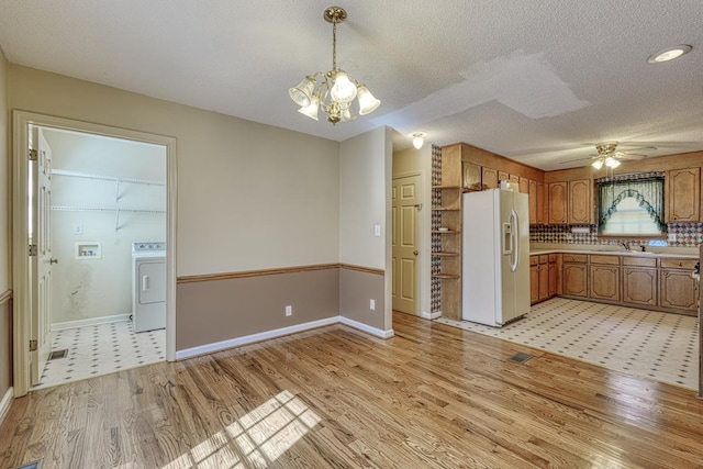 kitchen featuring white refrigerator with ice dispenser, brown cabinets, washer / clothes dryer, light countertops, and light wood-style floors