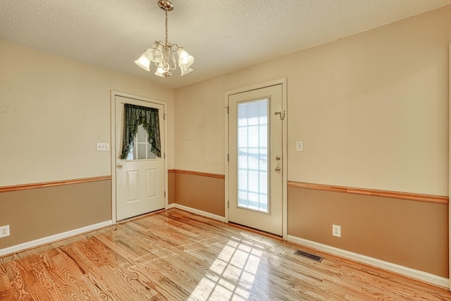 entryway with a textured ceiling, baseboards, wood finished floors, and a notable chandelier