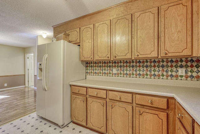 kitchen with a textured ceiling, white fridge with ice dispenser, light floors, and light countertops