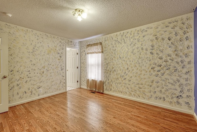 unfurnished room featuring visible vents, a textured ceiling, wood finished floors, baseboards, and wallpapered walls