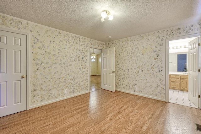 unfurnished bedroom with a textured ceiling, light wood-style floors, baseboards, and wallpapered walls