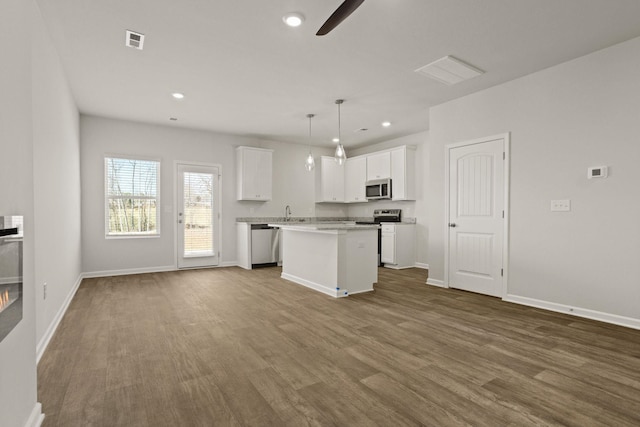 kitchen featuring dark wood-style flooring, a kitchen island, white cabinets, open floor plan, and appliances with stainless steel finishes