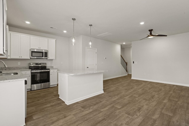 kitchen with a sink, a kitchen island, white cabinets, appliances with stainless steel finishes, and dark wood finished floors