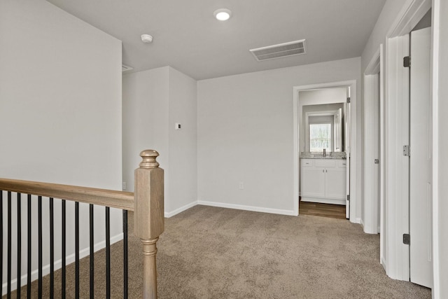 corridor with a sink, an upstairs landing, visible vents, baseboards, and carpet