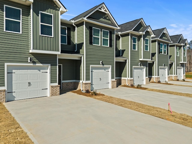 view of property with an attached garage, driveway, board and batten siding, and brick siding