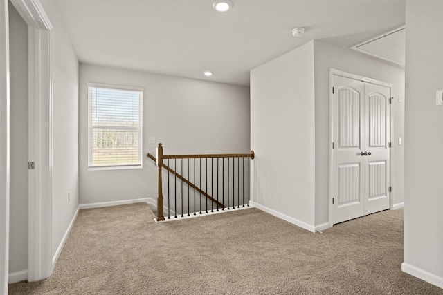 hallway featuring baseboards, carpet, an upstairs landing, and attic access