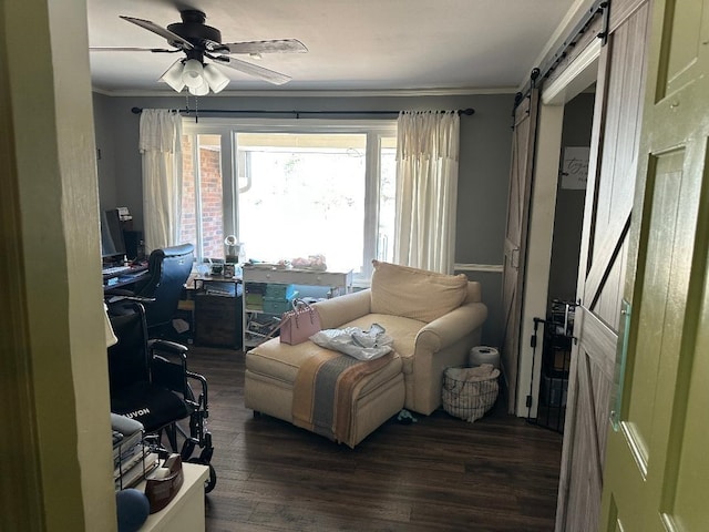 home office with a barn door, a ceiling fan, crown molding, and wood finished floors