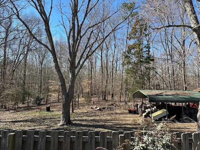 view of yard featuring a detached carport, fence, and a forest view