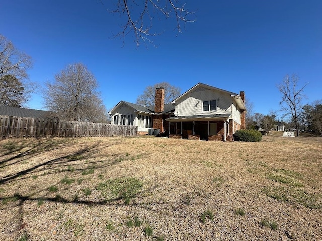 back of house featuring cooling unit, a sunroom, fence, and a chimney