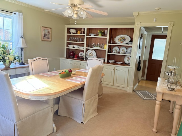 dining space with ceiling fan, ornamental molding, and light colored carpet