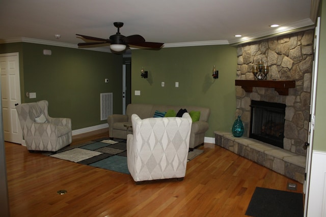 living room with a stone fireplace, wood finished floors, visible vents, and crown molding