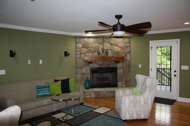 living room featuring baseboards, a ceiling fan, ornamental molding, wood finished floors, and a stone fireplace