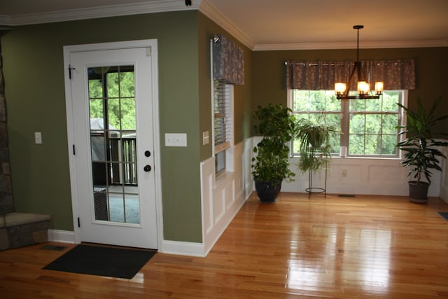 entrance foyer with a notable chandelier, light wood-style floors, ornamental molding, and a healthy amount of sunlight