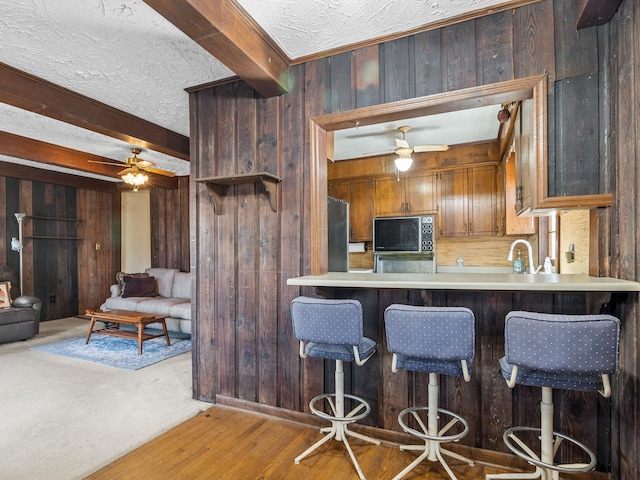 kitchen with a textured ceiling, wood walls, a ceiling fan, freestanding refrigerator, and beam ceiling