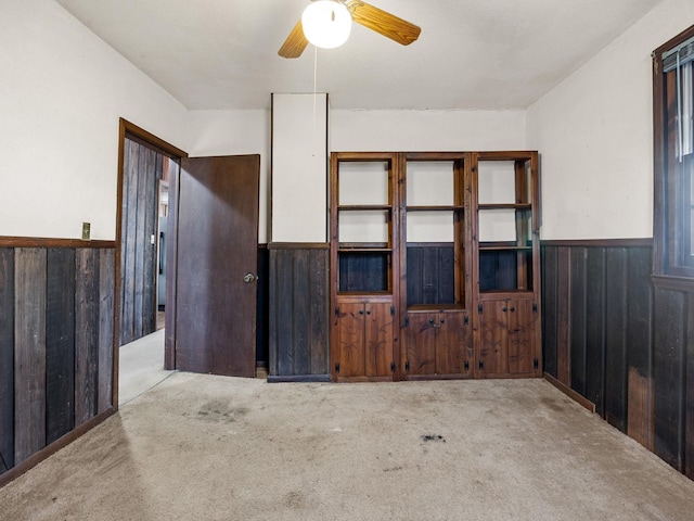 empty room featuring carpet, wood walls, wainscoting, and a ceiling fan