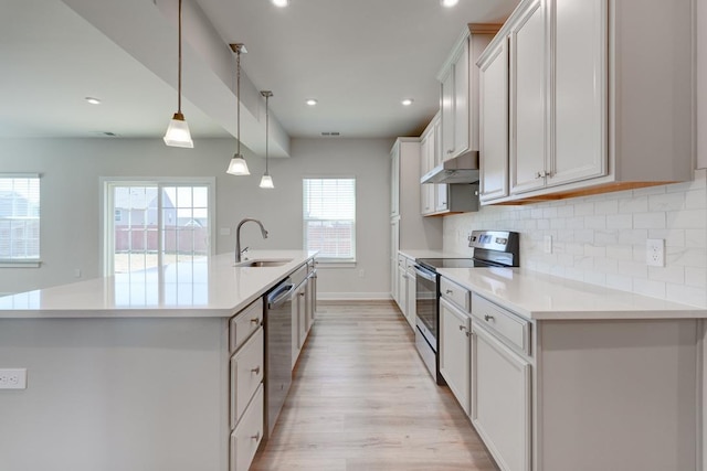 kitchen with backsplash, appliances with stainless steel finishes, a sink, an island with sink, and under cabinet range hood