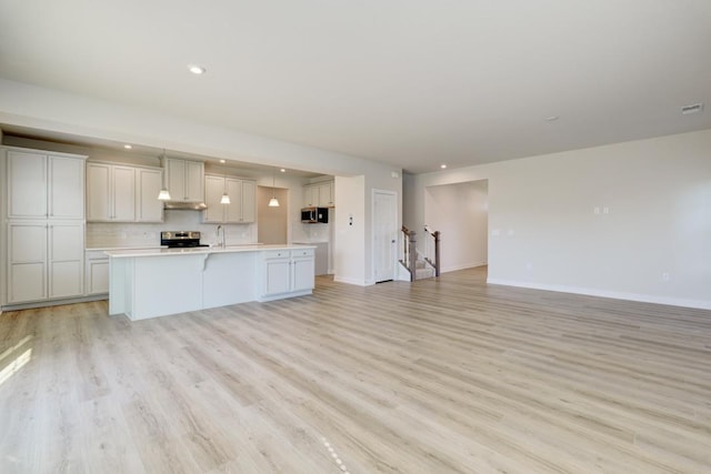 kitchen featuring light wood-type flooring, stainless steel appliances, light countertops, and open floor plan