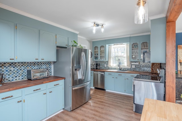 kitchen featuring light wood finished floors, butcher block countertops, ornamental molding, stainless steel appliances, and a sink