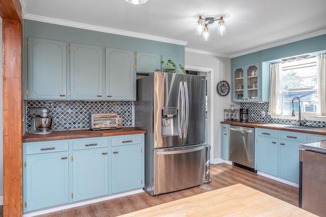 kitchen featuring a toaster, appliances with stainless steel finishes, light wood-style floors, ornamental molding, and glass insert cabinets