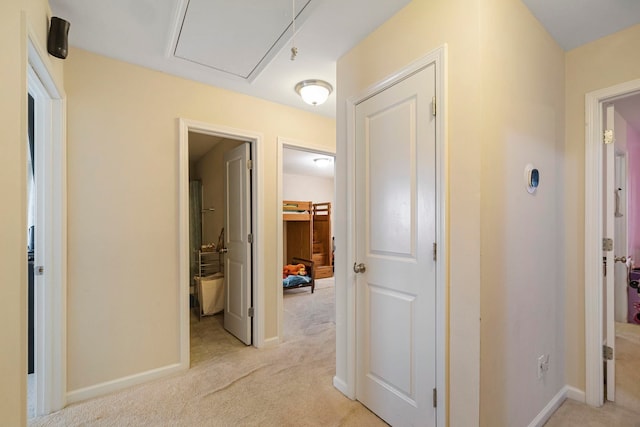 hallway featuring light carpet, attic access, and baseboards