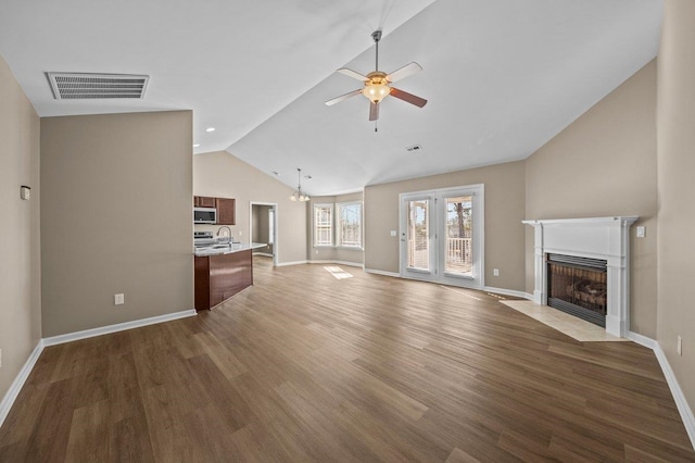 unfurnished living room featuring visible vents, a fireplace with flush hearth, a sink, wood finished floors, and ceiling fan with notable chandelier