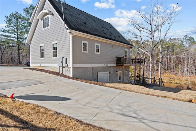 view of side of home featuring a shingled roof, concrete driveway, and a wooden deck