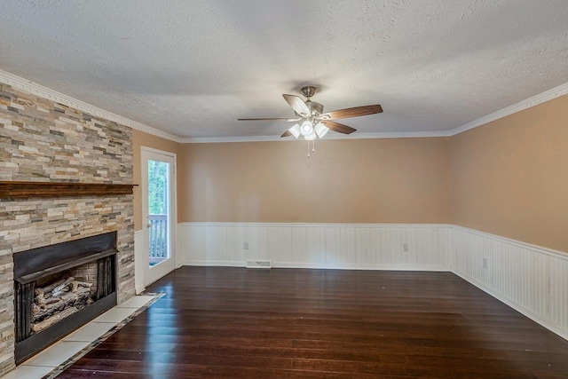 unfurnished living room featuring a textured ceiling, a stone fireplace, a wainscoted wall, wood finished floors, and visible vents