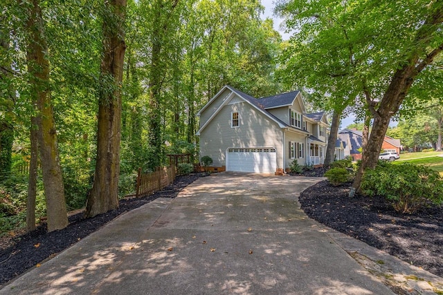 view of side of property featuring concrete driveway, an attached garage, and fence