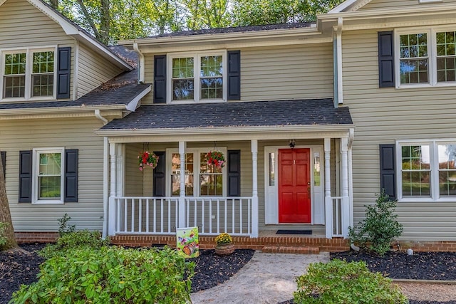 view of exterior entry with a porch and roof with shingles