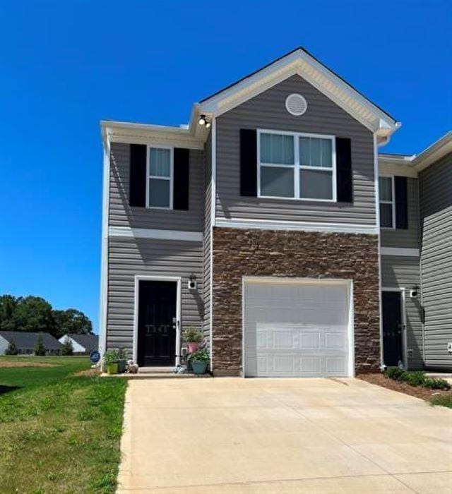 view of front of property featuring stone siding, driveway, an attached garage, and a front lawn