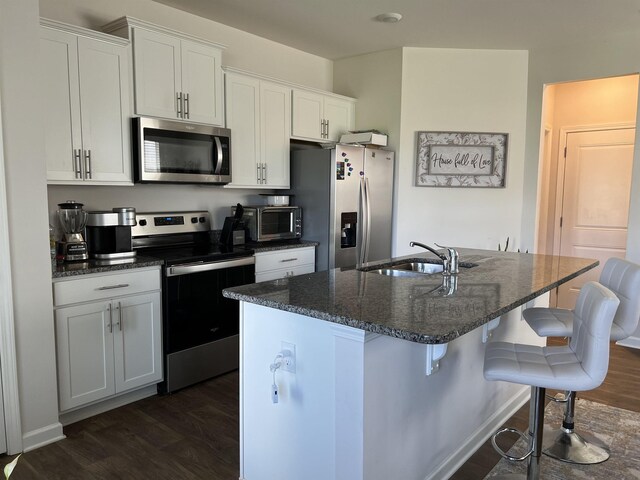 kitchen featuring a center island with sink, a sink, a kitchen breakfast bar, appliances with stainless steel finishes, and dark wood-style flooring