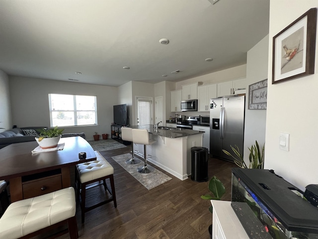 kitchen with open floor plan, stainless steel appliances, dark wood-style floors, white cabinetry, and a sink