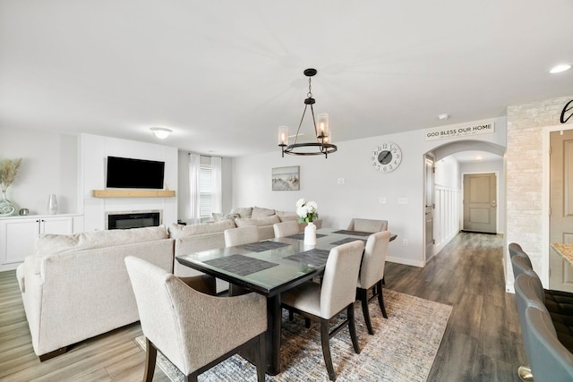 dining area with arched walkways, wood finished floors, a glass covered fireplace, and baseboards