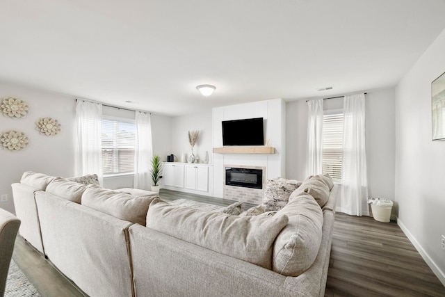 living room featuring wood finished floors, a glass covered fireplace, visible vents, and baseboards