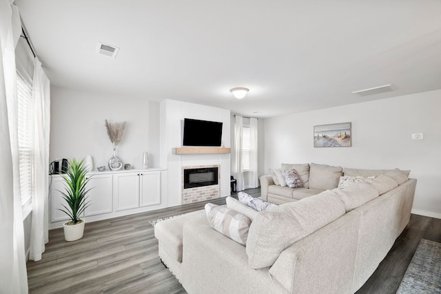 living room with wood finished floors, a glass covered fireplace, and visible vents