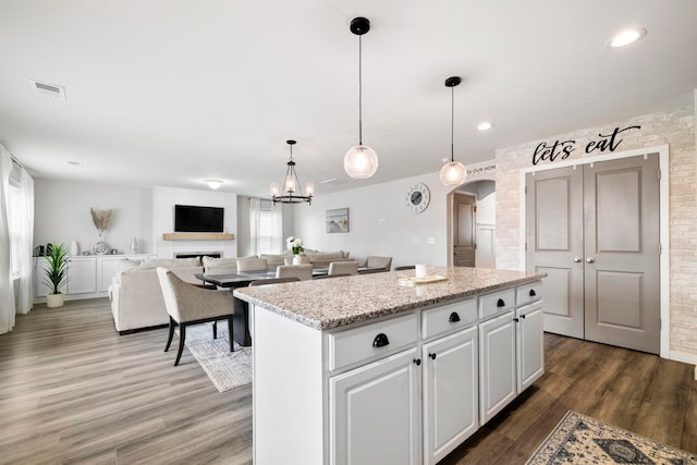 kitchen featuring arched walkways, a fireplace, wood finished floors, a kitchen island, and visible vents