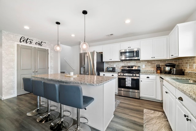 kitchen with decorative backsplash, dark wood finished floors, appliances with stainless steel finishes, a center island, and a sink