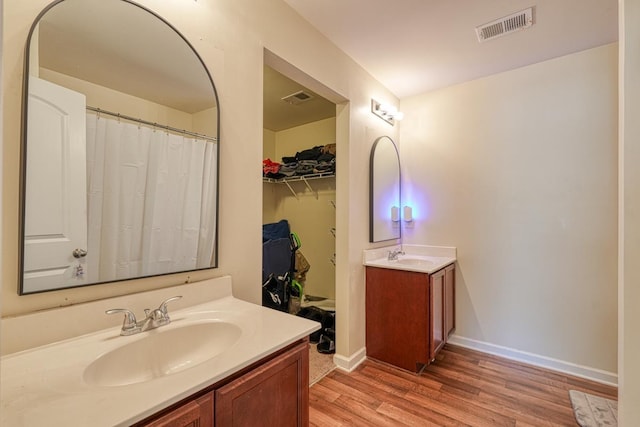 bathroom featuring visible vents, two vanities, a sink, and wood finished floors