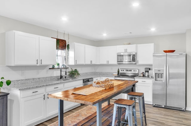 kitchen with stainless steel appliances, light wood-style flooring, a sink, and white cabinetry