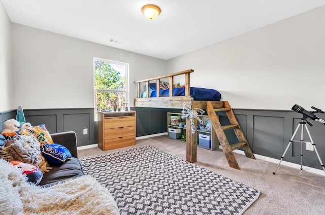 bedroom with a wainscoted wall, carpet flooring, visible vents, and a decorative wall