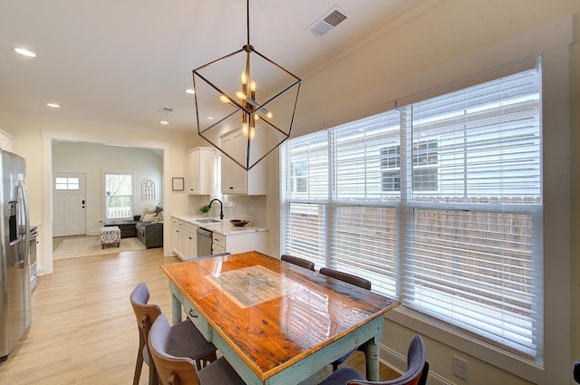 dining area featuring ornamental molding, light wood-style flooring, visible vents, and an inviting chandelier