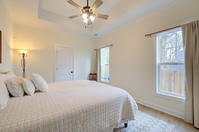 bedroom featuring ceiling fan, baseboards, a tray ceiling, light wood finished floors, and crown molding