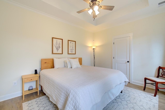 bedroom with baseboards, a raised ceiling, visible vents, and light wood-style floors